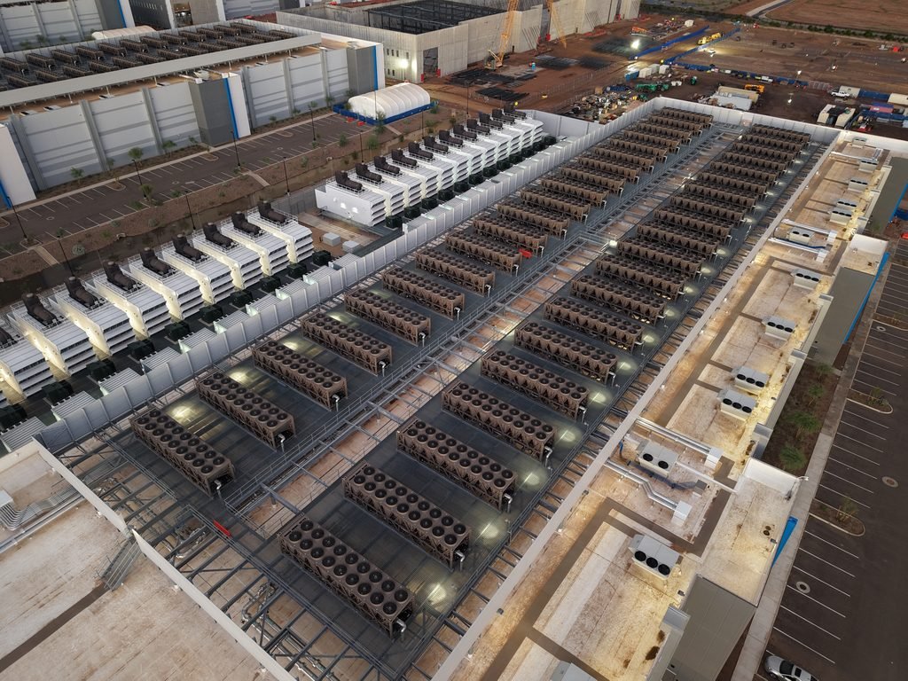 Aerial photo of a large data centre roof lined with rows of cooling units, with backup generators along the building edge